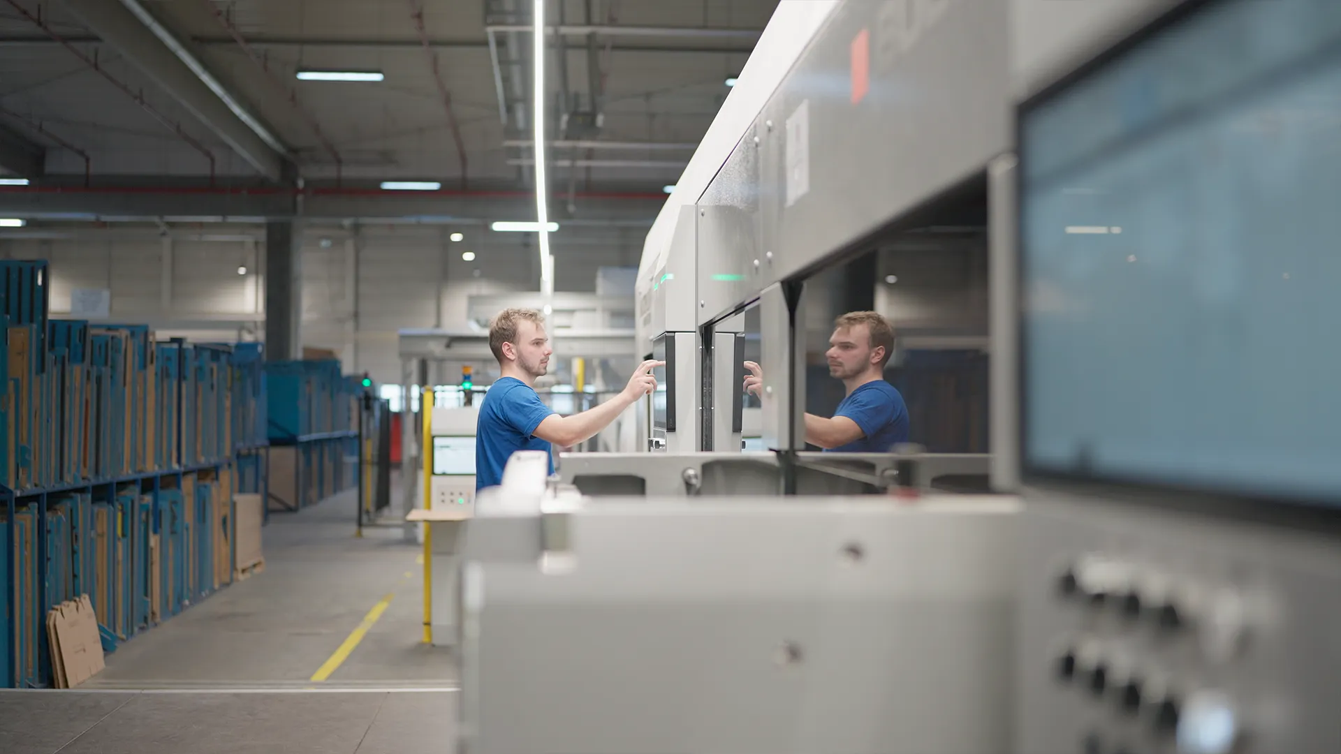 Operatore imposta un lavoro dal touchscreen della fustellatrice BOBST, riflesso nel vetro